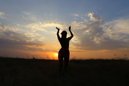 Female with beautiful figure takes yoga postures, gymnastics and ballet spends stretching and meditating, posing for advertising shoot fitness studio, healthy energy drink, dancing belly dancing among wide field on background of yellow sunset and beautifuの写真素材