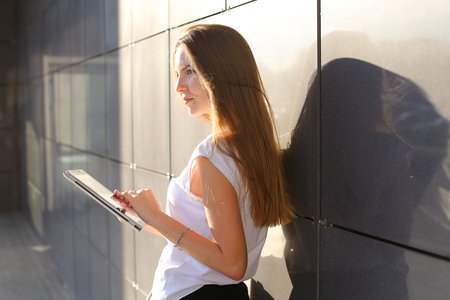 Female work, negotiating, solves problems, browsing touch looking tablet. Young beautiful business woman entrepreneur with long hair wearing suit standing near center technology sun.の写真素材