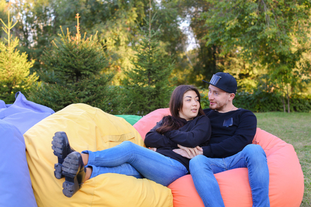 Pair of lovers of young attractive people sitting in soft yellow and red chair.  Young people cute communicate, plan to travel, choosing interior of apartment, guy tells about one of following general recreation, boyfriend and girlfriend smiling, hugging の写真素材