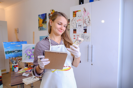 Female European appearance painter talking on mobile with clients, solve problems, appointments with students and posing for advertising art appliances or art school, order paint, canvas or frame.Woman With Long Light Brown Hair Dressed Sht Pale Purple blの写真素材
