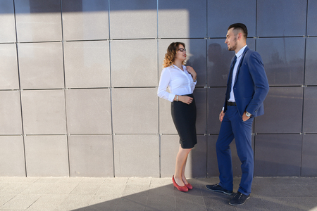 Attractive woman and man, young entrepreneurs, students and friends discuss important issues, share business ideas, smiling, laughing, make decisions, solve problems and stand next to each other near  gray wall of business center outdoors. One of guys dreの写真素材