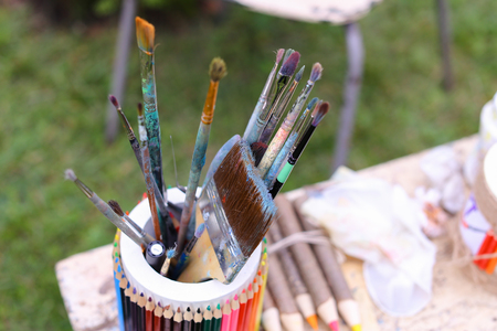 Photo shows thin and thick brush for oil and acrylic paints that in colored pencils and stands with other artistic objects that lie on gray table in park in open air. Concept of art materials store advertising art tools and paints, hobby and interests.の写真素材