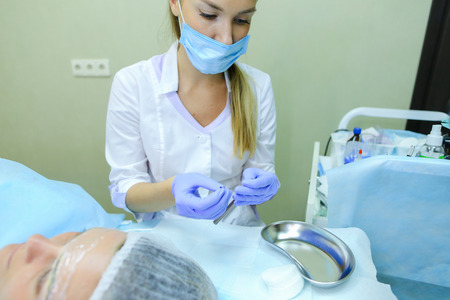 Blonde girl European appearance, professional engaged in reconstruction of eyebrows responsibly preparing to start work mikrobleyding eyebrows, eyebrows customer focused prepares women to paint application, choose appropriate shade for tattoo, next to couの写真素材