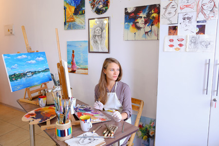 Charming Young Woman Artist Draws Oil Painting With Purple Flowers on a White Canvas, Female Enjoying Favorite Work, Hobbies, posing  for camera and Painting Picture to Order or Gift. Woman With Long Light Brown Hair Dressed Sht Pale Purple Jacket, White の写真素材