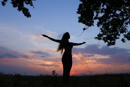 Female with beautiful figure takes yoga postures, gymnastics and ballet spends stretching and meditating, posing for advertising shoot fitness studio, healthy energy drink, dancing belly dancing among wide field on background of pink sunset and beautiful の写真素材