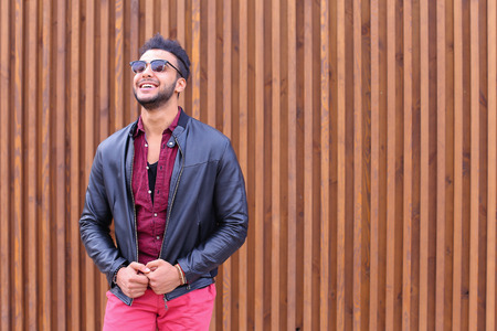 Attractive Arabic Man Young Adult Businessman Poses For Photograph, Preening For Meeting With Girlfriend, Straightens Hair and Jacket, Smiles and Looks Away in Background of Wooden Panel Stairs Outdoors. Stylish Young Man With Dark Hair and Sunglasses Dreの写真素材