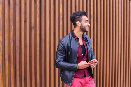 Young Arab pleasant appearance reads and writes message, smiling looking to side, makes appointment and looks forward to important person, smiling guy posing and shooting for advertising mens contemporary clothing or mobile phone brand mobile phone operatの写真素材