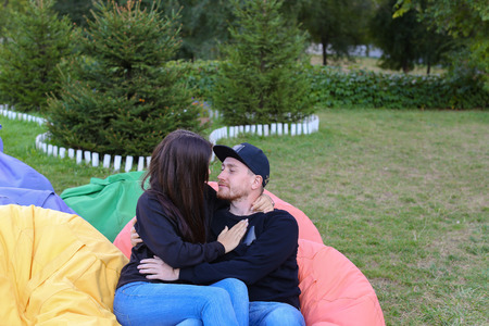 Pair of lovers of young attractive people sitting in soft yellow and red chair.  Young people cute communicate, plan to travel, choosing interior of apartment, guy tells about one of following general recreation, boyfriend and girlfriend smiling, hugging の写真素材