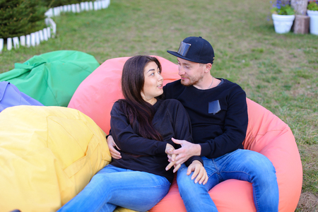 Pair of lovers of young attractive people sitting in soft yellow and red chair.  Young people cute communicate, plan to travel, choosing interior of apartment, guy tells about one of following general recreation, boyfriend and girlfriend smiling, hugging の写真素材