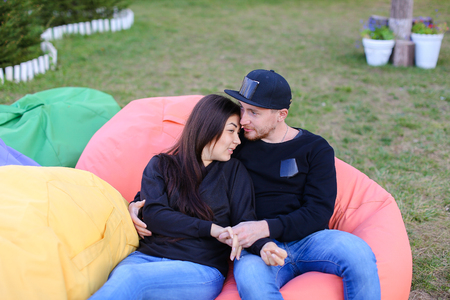 Pair of lovers of young attractive people sitting in soft yellow and red chair.  Young people cute communicate, plan to travel, choosing interior of apartment, guy tells about one of following general recreation, boyfriend and girlfriend smiling, hugging の写真素材