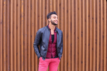 Charismatic Young Businessman Muslim Man Comes Closer to Camera, Smiles and Poses For Camera on Photographer, Shows Gestures, Laughs, Advertises Clothing on Wooden Panel Background Stairs Outdoors. Stylish Young Man With Dark Hair and Sunglasses Dressed iの写真素材