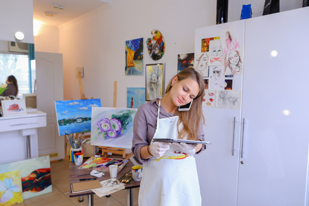 Female European appearance painter talking on mobile with clients, solve problems, appointments with students and posing for advertising art appliances or art school, order paint, canvas or frame.の写真素材