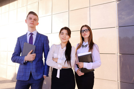 Modern handsome male man and two pretty confident girl, successful young office workers, businessmen, students holding in hands documents, smiling and posing to photographer camera, taking pictures for company brochures, advertising office clothes and staの写真素材
