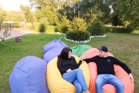 Pair of lovers of young attractive people sitting in soft yellow and red chair.  Young people cute communicate, plan to travel, choosing interior of apartment, guy tells about one of following general recreation, boyfriend and girlfriend smiling, hugging の写真素材