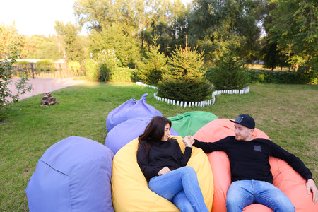 Pair of lovers of young attractive people sitting in soft yellow and red chair.  Young people cute communicate, plan to travel, choosing interior of apartment, guy tells about one of following general recreation, boyfriend and girlfriend smiling, hugging の写真素材
