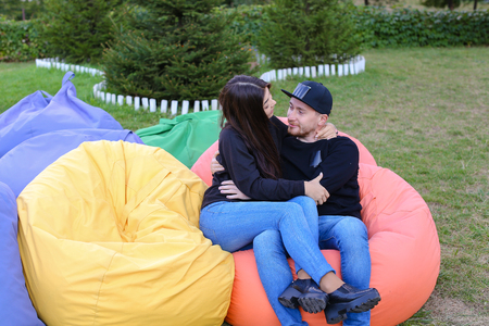 Pair of lovers of young attractive people sitting in soft yellow and red chair.  Young people cute communicate, plan to travel, choosing interior of apartment, guy tells about one of following general recreation, boyfriend and girlfriend smiling, hugging の写真素材