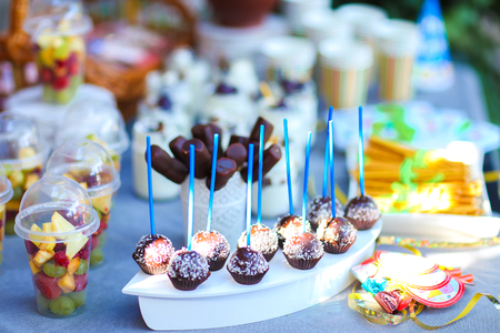 In photo depicts variety of goodies, delicious food, clear jars with cottage cheese soufflÃÂ© with layer of pastry topped with fruit and straws, chocolate long candy skewers in patterned white small vase, chocolate balls in coconut flakes with blue strawの写真素材