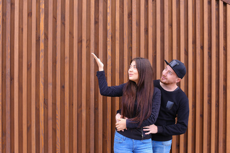 Bride and groom embracing each other, looking to sky and come up forms of clouds, dreaming about future together, enjoy each others arms, will not hurry and rest, stand near wooden walls of restaurant outdoors. Man dressed in black sweater, blue jeans, snの写真素材