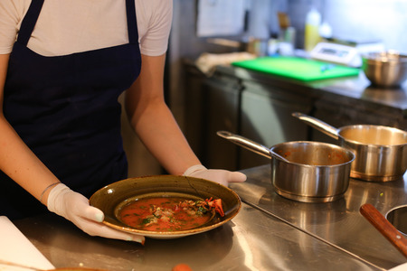 Girl female woman chef prepares dishes in the restaurant, pours into a bowl, gloved hands, a kitchen for cookingの写真素材