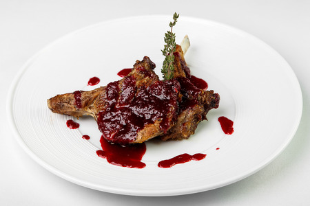 Juicy piece of lamb under red berry sweet and sour sauce and sprinkled with spices and herbs on large round white plate on white background. Concept is delicious and beautiful food, restaurant supply of snacks and main dishes, useful and good nutrition, pの写真素材