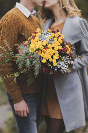 Flower bouquet on background of coupleâ??s love, affection. Boy and girl of European appearance with warm clothes, pictures with soft background bokeh blur fall. Concept of happiness, joy, endless love. Focus on flowersの写真素材