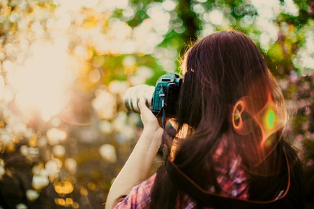Young photographer with long hair takes picture with camera outside with summer sun lightの写真素材