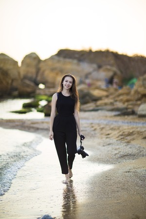 Young woman photographer holding camera and looking into frame. Girl dressed in black jumpsuit, European appearance. Concept of feminine beauty,  work photographer tourist with camera on vacation or trip.の写真素材