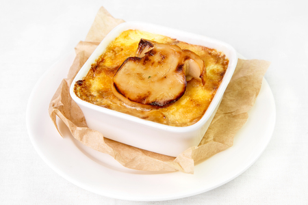 Appetizing gratin, baked in certain way fish or meat with vegetables with cheese golden crust in square deep plate of white color that stands on sheet of parchment and on white round plate on light background. Concept useful delicious and beautiful dishesの写真素材