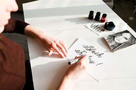 Creative female holds black marker in hands and writes in beautiful italic font inscription "Black Friday" on white cardの写真素材