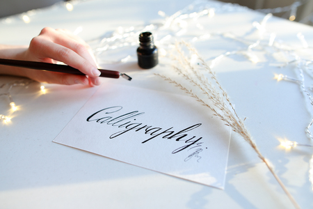 Girl calligrapher holds in hand wooden rod with pen for writing and dunks in black ink for writing...
