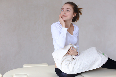 Cute young woman looks away and touches face, smiles and pleased with result of cosmetic procedureの写真素材
