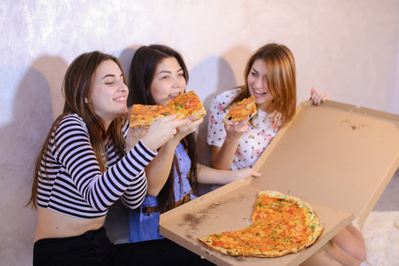 Three wonderful women having fun, ordered large fragrant pizza and try, laughing and talking on girlish themes.の写真素材