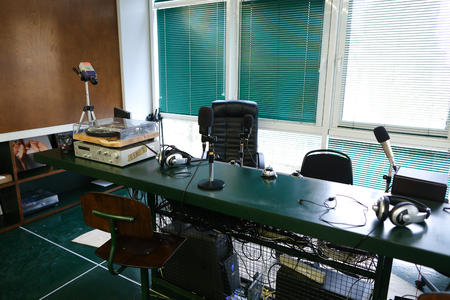 Taking Close-up in studio. Devices for recording of radio microphones and mixing consoles, broadcast processor and special devices on wooden table in radio studio with big windows ponoramic. Concept of radio studio and online broadcast, equipment device rのeditorial素材