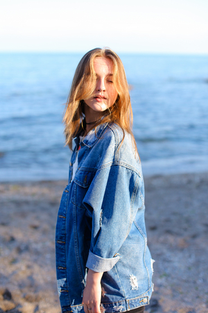 Charming girl resting and with beautiful smile on face posing in camera, laughing and enjoying beautiful day on shore of blue sea.の写真素材