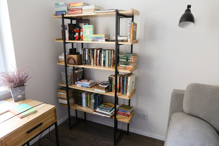 Details of interior of office in bright and spacious room. In room minimalist bookcase with wooden shelves and black metal opals on which there large number of scientific and general educational books with magazines. Cabinet with large white window and whのeditorial素材