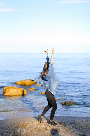 Sweet woman walks and poses in camera, smiles and laughs widely, raises hands up and starts happily whirling on spot, taking off jacket from shoulders. European-looking girl with medium-length blond hair dressed in black pants, white T-shirt with bright pの写真素材