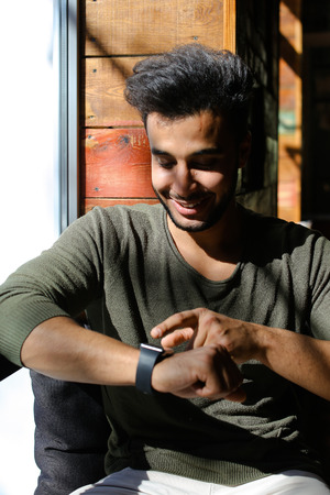 Arabian sits near window and uses smart watch in caf . Person dressed in khaki pullover and white jeans.の写真素材