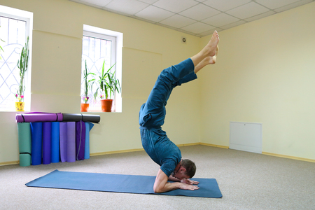 Young brunette of American origin sits on yoga mat and performs longitudinal twine. Short-haired...