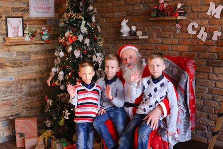 Merry brothers boys sitting on Santa Clauss lap and waving their palms camera rejoice.の写真素材