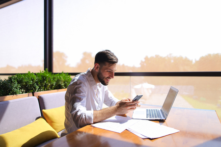 Caucasian real estate broker speaking by smartphone with customer and using laptop.の写真素材