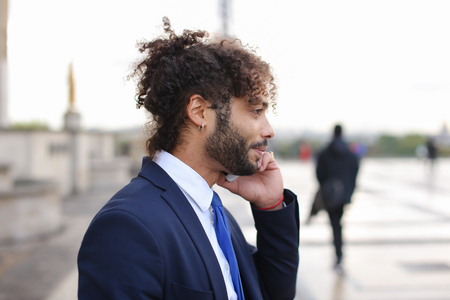 Attractive businessperson calling cooperator and disputing by phone with Eiffel Tower in background in. Young man making official journey to France. Concept of works debating and detached duty to Europe.の写真素材