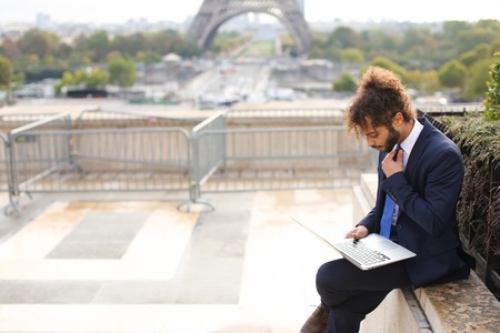 Mulatto man using laptop on open air around Eiffel Tower in slow motion.の写真素材