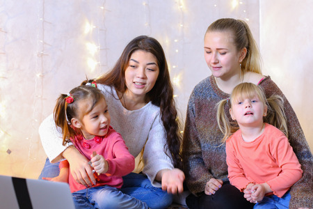 Two young and beautiful older girls together with two younger children of girls watch cartoons or movies on computerの写真素材