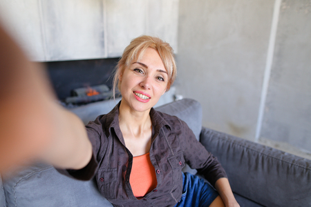 Attractive young woman holding smartphone on outstretched hands and with smile on face posing and taking pictures of herselfの写真素材