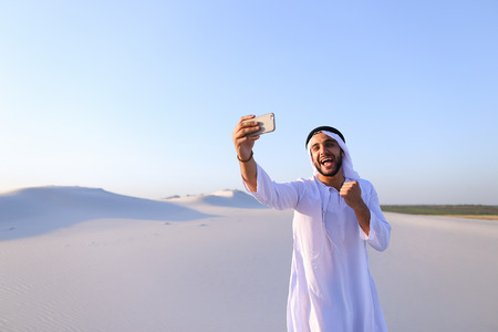 Happy, handsome guy, emirate and tourist, conducts dialogue through Internet with help of deviceの写真素材