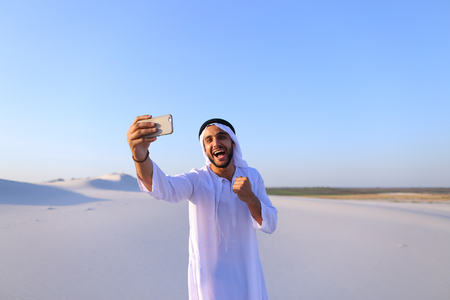 Happy, handsome guy, emirate and tourist, conducts dialogue through Internet with help of deviceの写真素材