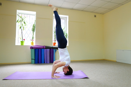 Beautiful dark-haired woman sits on floor on yoga mat and performs stretching exercises.の写真素材