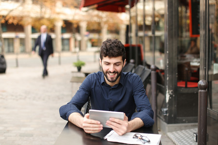 Dissatisfied man losing at online game playing with tablet at street cafe. Young man has dark hair, brown eyes and beard. Concept of excitement loss and Internet entertainments.の写真素材