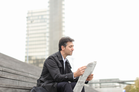 effect. Tutor dressed in gray coat sitting on rung and read morning newspaper. Articles pleased man and caused smile. Male turn edition for read any good news. Concept of positive emotions from good news.の写真素材