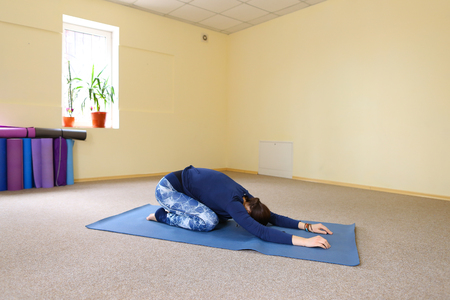 Sportswoman focused on stretch before Pilates class. Girl doing warm up for legs on mat. Female has hair pulled back, concentrated look. Athlete dressed in dark top, yoga legging trains in fitness room. Concept of online training, customizable workouts.の写真素材